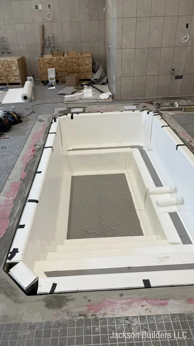 Fiberglass pool shell being set into a tiled indoor pool room — Jackson Builders project photo 1