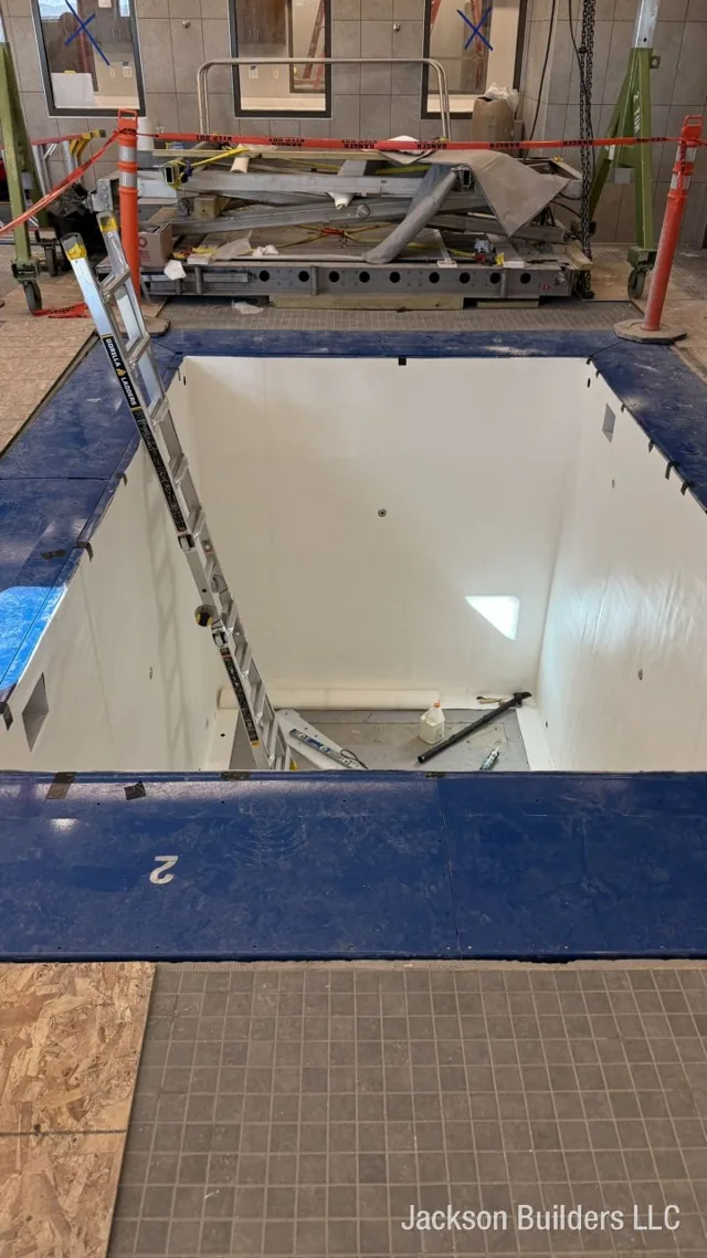 Fiberglass pool shell being set into a tiled indoor pool room — Jackson Builders project photo 2